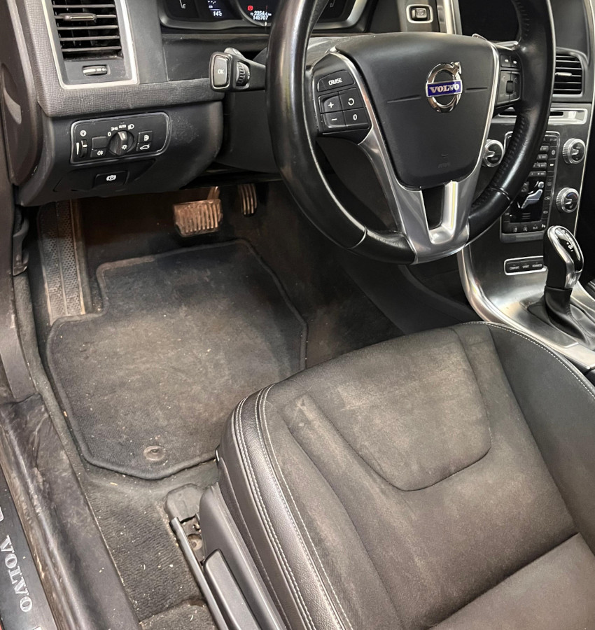 Interior sucio de coche turismo Volvo, con el salpicadero, asientos y alfombrillas sucios.